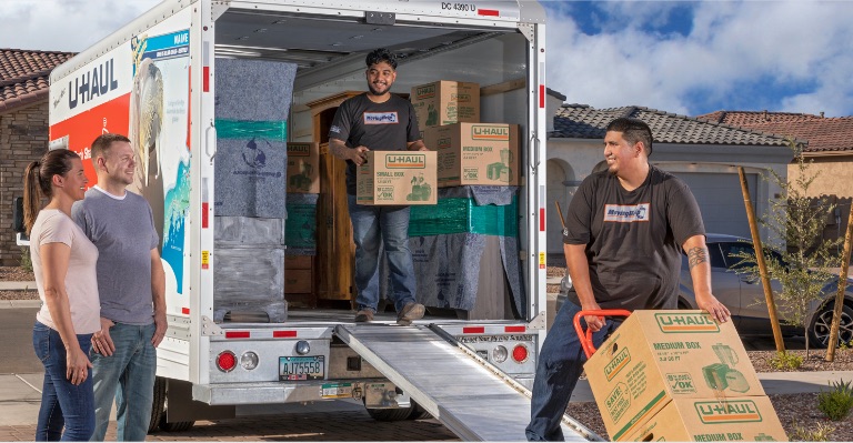 Movers loading boxes onto a U-Haul® truck with a moving dolly in front of customers