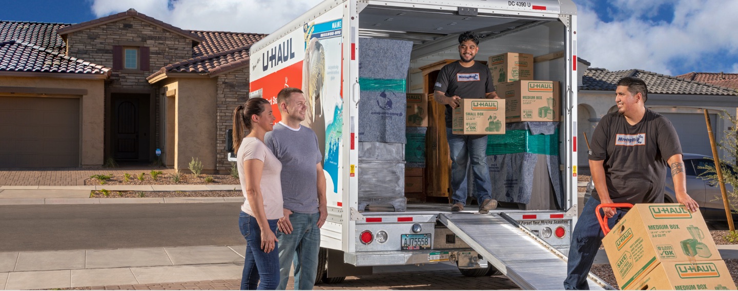 Movers loading boxes onto a U-Haul® truck with a moving dolly in front of customers