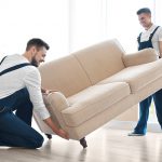 Two helpers begin to place a couch inside a home. Hiring a moving labor company costs money, but with Moving Help, it won’t cost as much as you think.