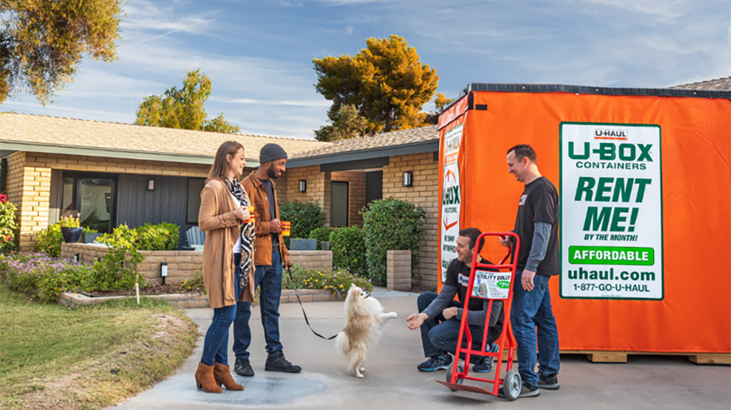 Couple standing on driveway near movers and a U-Box container.