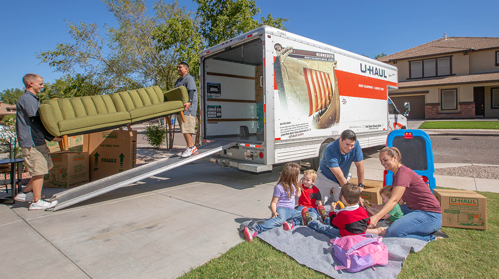 A family plays on their lawn as Service Providers unload their couch.