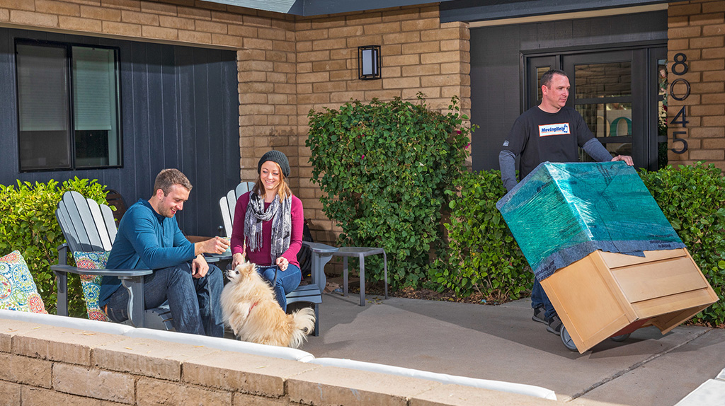 Two customers relax with their dog as a Moving Helper pushes a dolly that’s holding a dresser.