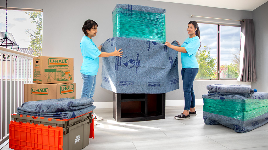 Two movers wrapping an armoire with blankets and stretch wrap.