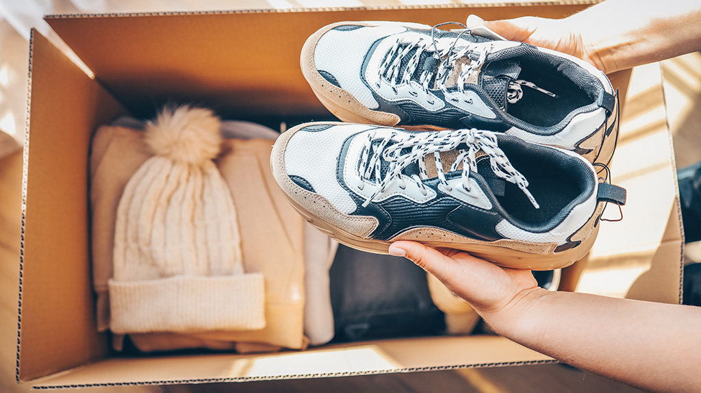 Man places tennis shoes into moving box with other clothing items.