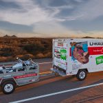 U-Haul rental truck tows a motorcycle along a desert highway.