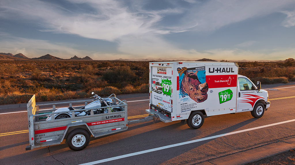 U-Haul rental truck tows a motorcycle along a desert highway.