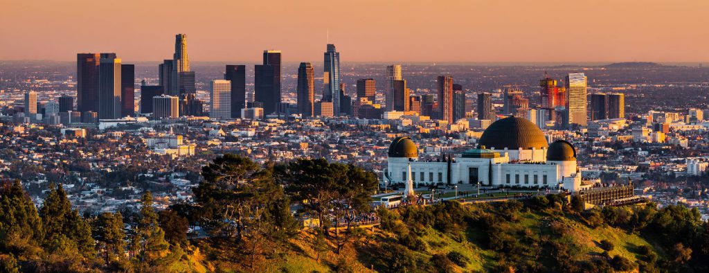 The Griffith Observatory and Los Angeles skyscrapers are visible during a summer sunset.