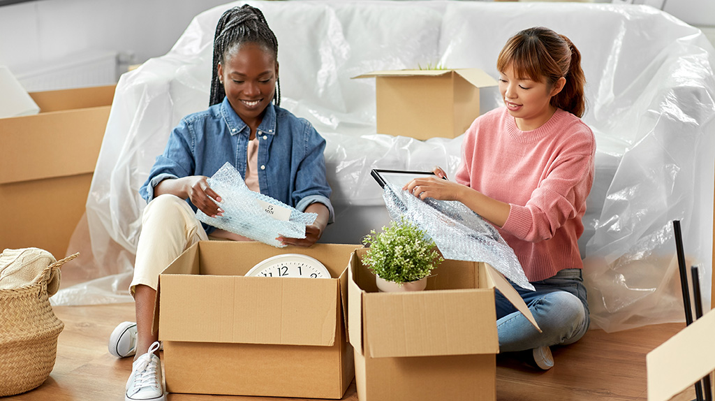 Two women begin packing items into a box before the big move.