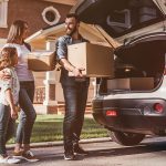 A family begins to pack boxes into their car as they prepare it with moving day essentials.