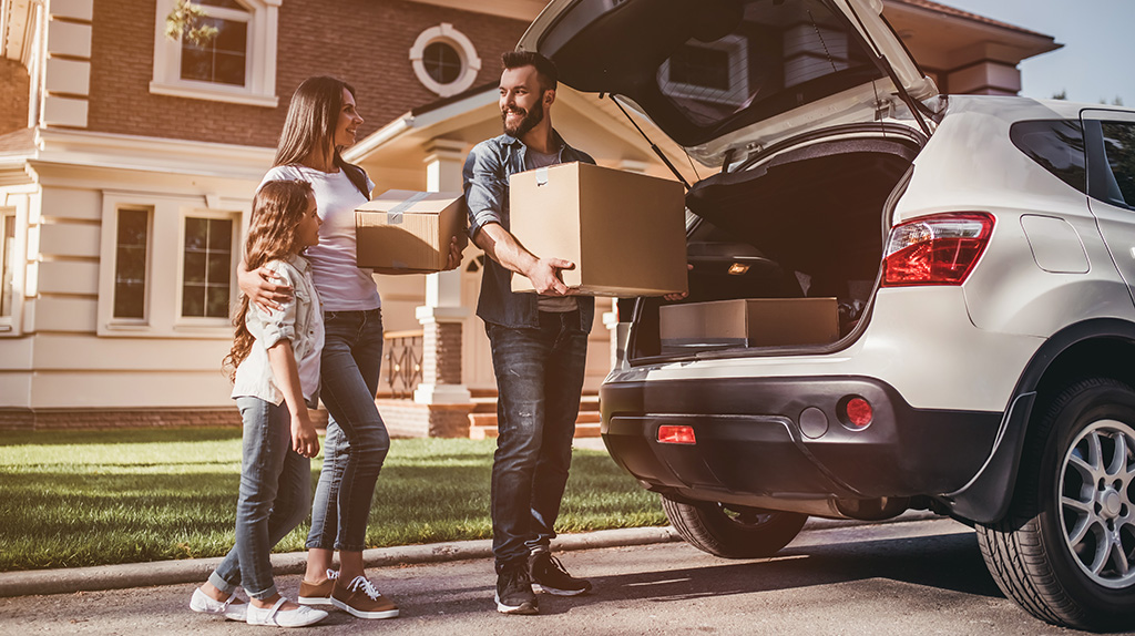 A family begins to pack boxes into their car as they prepare it with moving day essentials.
