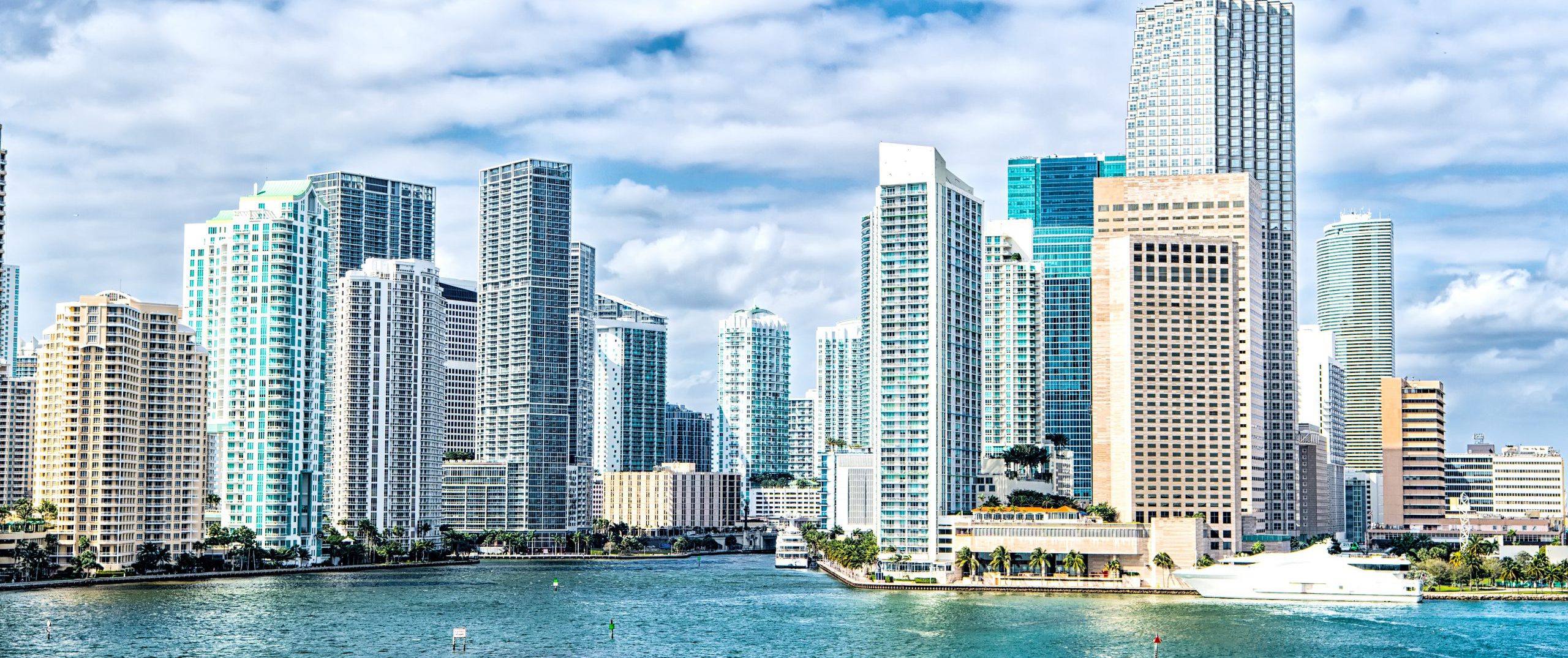 Miami can be seen on a beautiful, sunny afternoon with boats driving around on blue water along the coast.