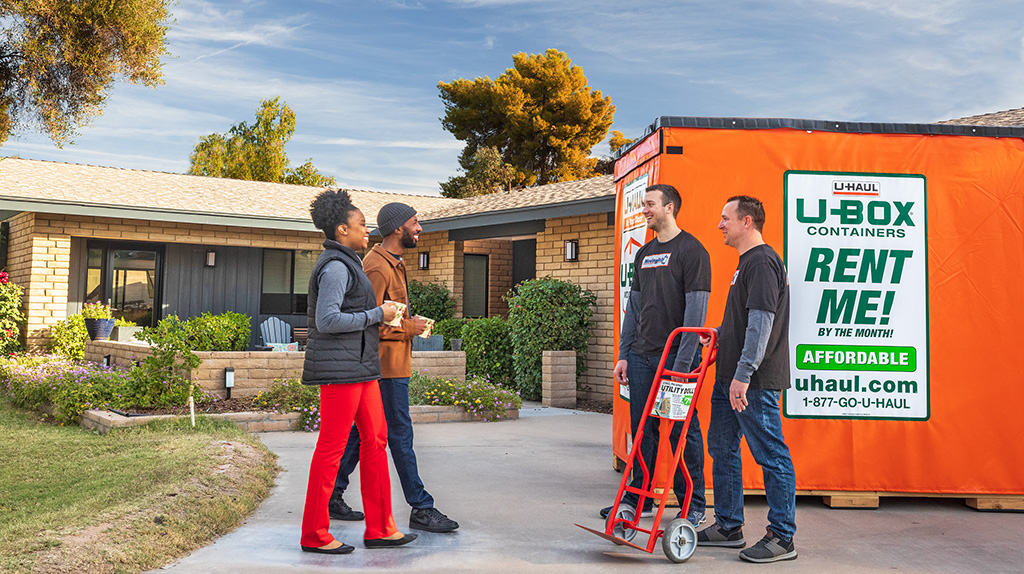 A couple stands with their local movers, who are holding a utility dolly provided for them.