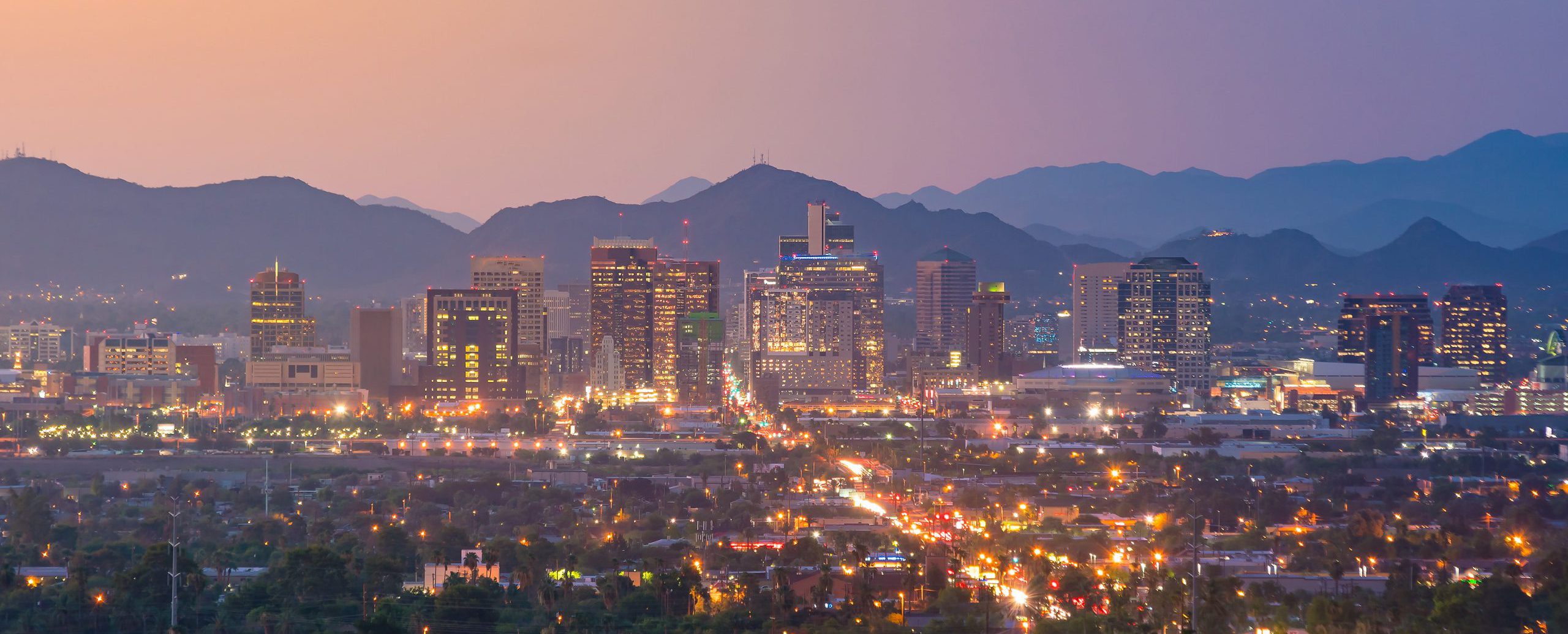 A wide panoramic shot of downtown Phoenix and the local mountains at sunset.
