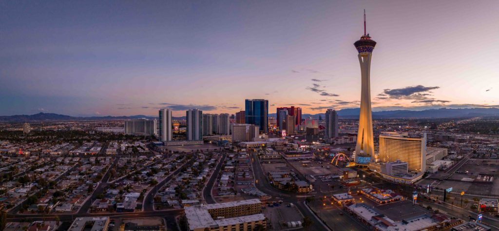 The Las Vegas downtown area can be seen as the sun begins to set. The STRAT Hotel, Casino & Skypod lights up in the foreground.