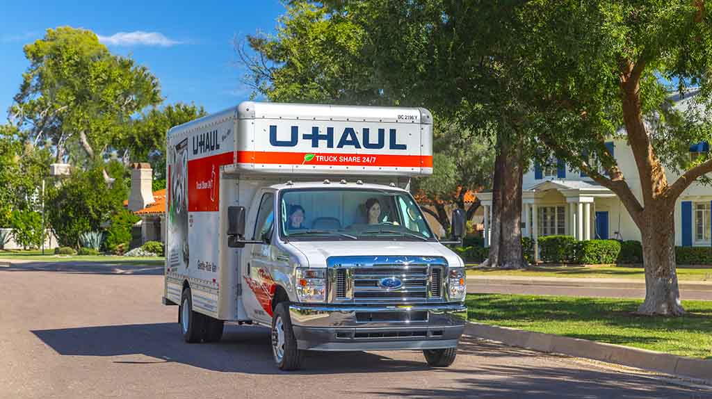 A customer drives a U-Haul truck rental down the road in a neighborhood.