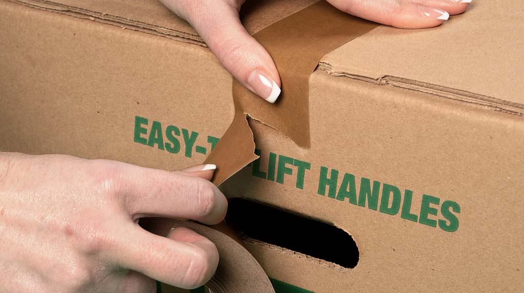 A customer easily rips a piece of paper packing tape for moving boxes before flatting the tape to the box.