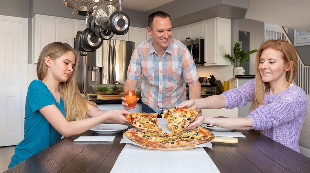 A family celebrates with pizza at the dinner table after moving into their new home.