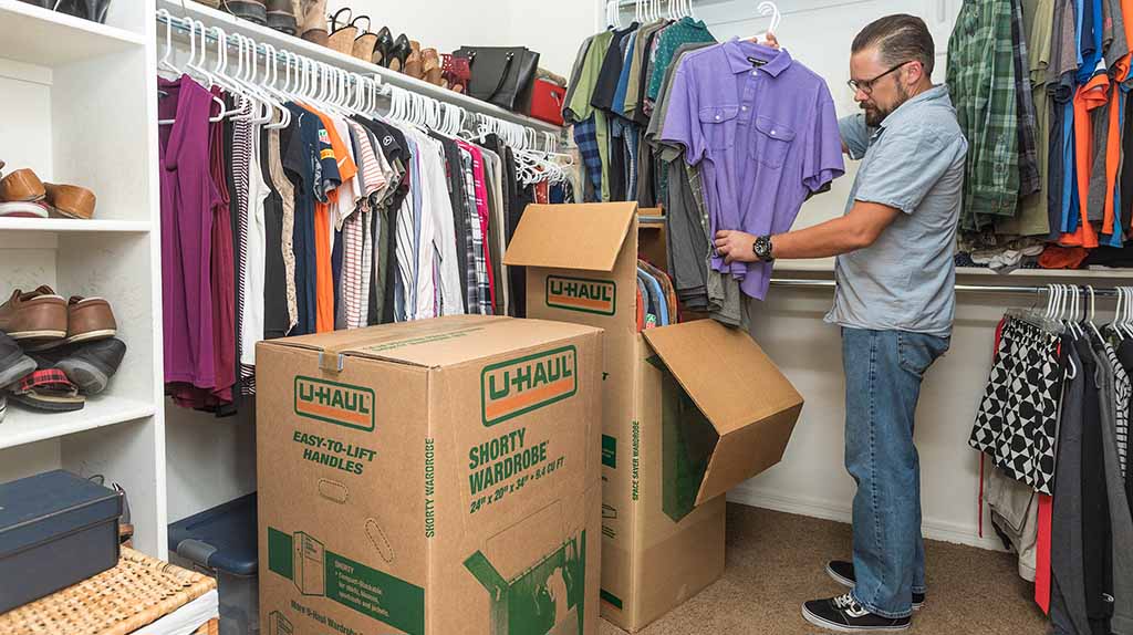 A man begins to start packing his collared T-shirts into a U-Haul wardrobe box.
