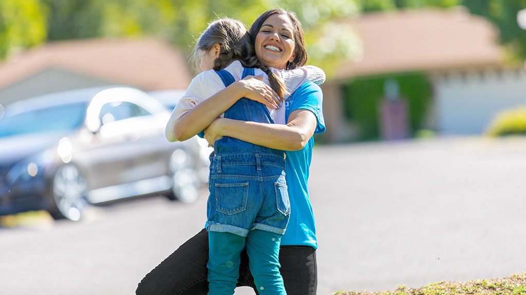 A mother hugs her daughter outside their new home after moving.