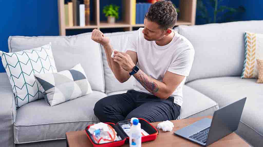 A man cleans a cut on his arm in his apartment. The Moving Help first apartment checklist will help prepare you by making sure you account for a first-aid kit.