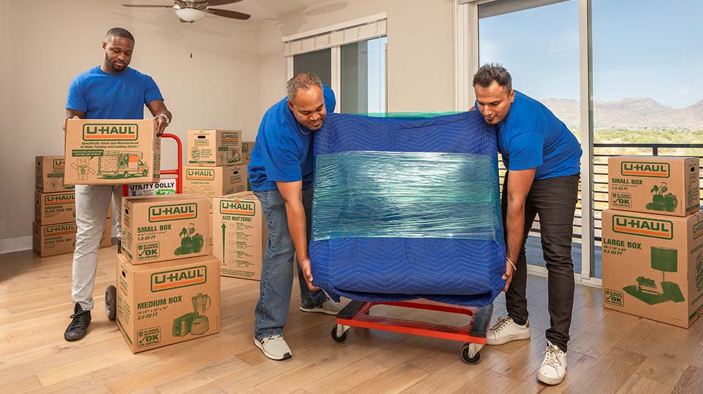 Three Moving Helpers prepare to load furniture and moving boxes onto dollies. The Moving Help first apartment checklist will guide you on what you might need for your apartment.
