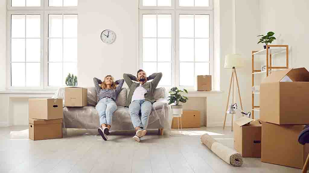 A man and a woman relax on their couch after moving some boxes into their first apartment.