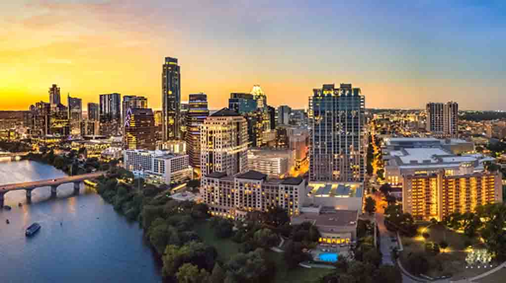 An aerial shot shows Austin’s downtown and the Colorado River as the sun begins to set.