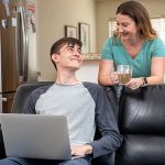 A teenage son looks at his mom while searching for college moving options on his computer.