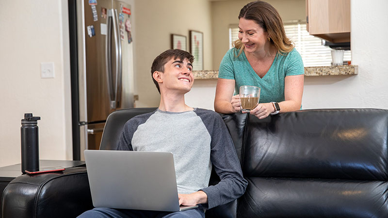 A teenage son looks at his mom while searching for college moving options on his computer.