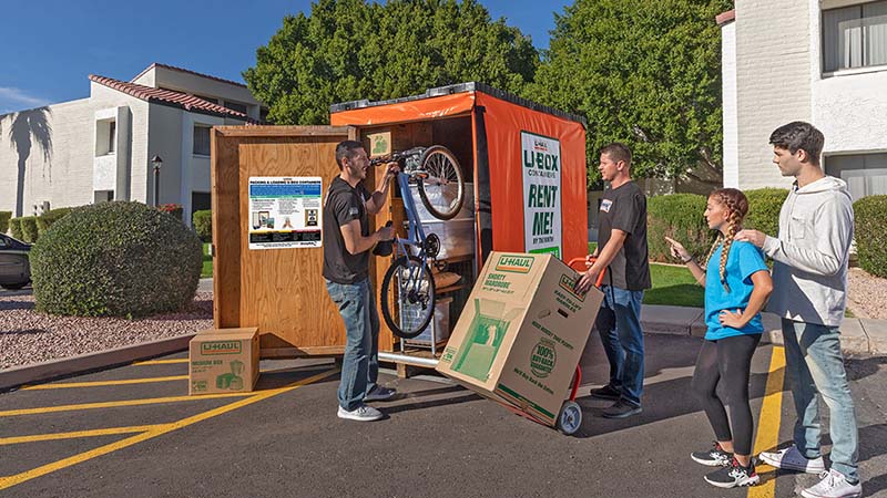 Two apartment moving labor providers begin to load a bicycle into a U-Box storage container.