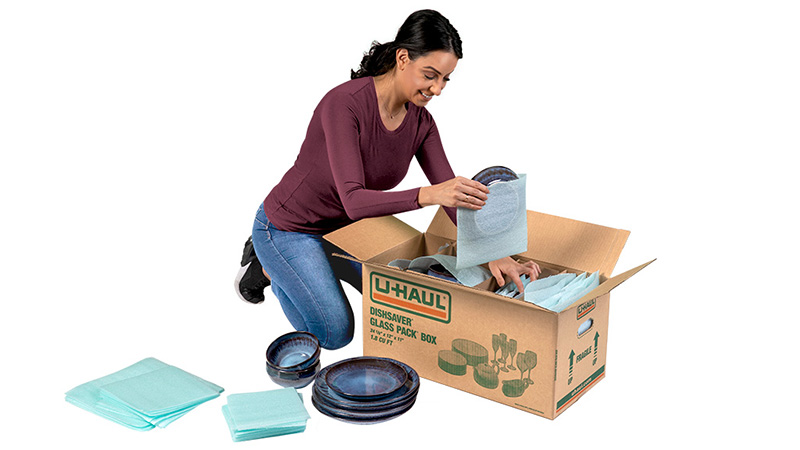 A woman starts packing dishes with a U-Haul dishes packing kit.
