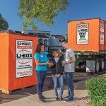 A U-Haul employee drops off a U-Box storage container for two customers while the rest of the U-Box containers sit on a truck.