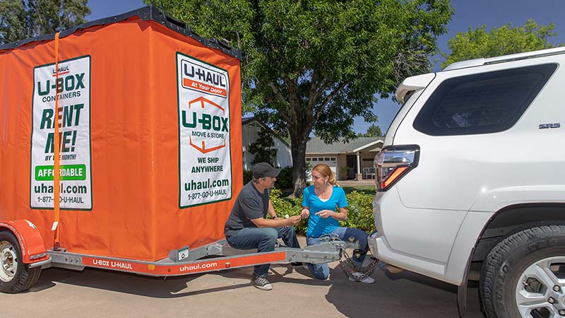 A man and a woman work together to hook a U-Box container on a trailer to their car.