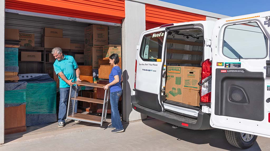 A man and a woman begin unloading their belongings from a cargo van and into a storage unit.