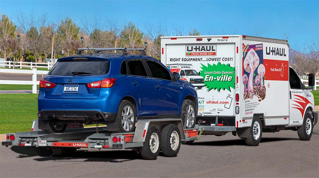 A customer drives a U-Haul truck rental with an auto transport carrying their car behind the truck rental.