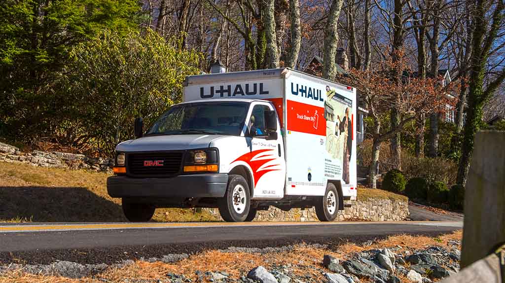 A customer drives a U-Haul truck rental down a road surrounded by trees.