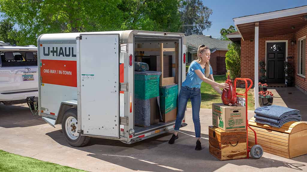 A customer pulls her belongings out a U-Haul utility trailer and places her items on the driveway of her home.