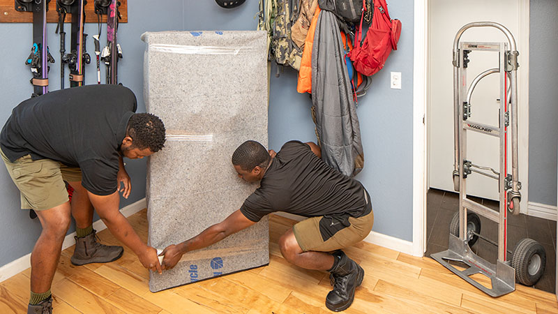 Two Moving Help moving labor providers prepare to protect a customer’s gun safe before placing it on a dolly.