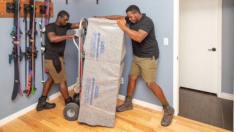 Two Moving Helpers work together to carefully place a gun safe onto a dolly for a customer.