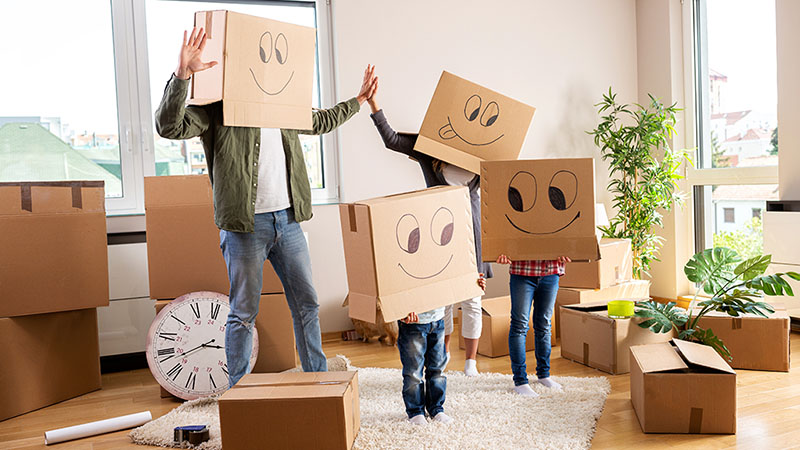 A family celebrates their new home by having fun with some moving boxes by placing them over their heads with smiley faces on the boxes.