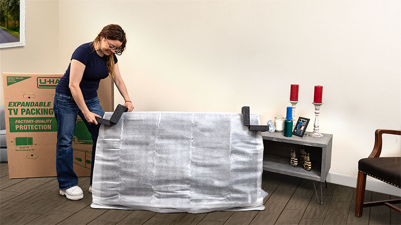 A woman carefully packs her TV using the ultimate TV packing kit from U-Haul. For a going away party, you could create a packing party for your friends and family.