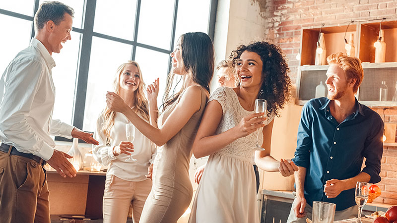 A ground of friends stand around laughing and mingling with one another at a going away party. A moving away party is a great way to connect with friends and family one last time before you move to your new home.