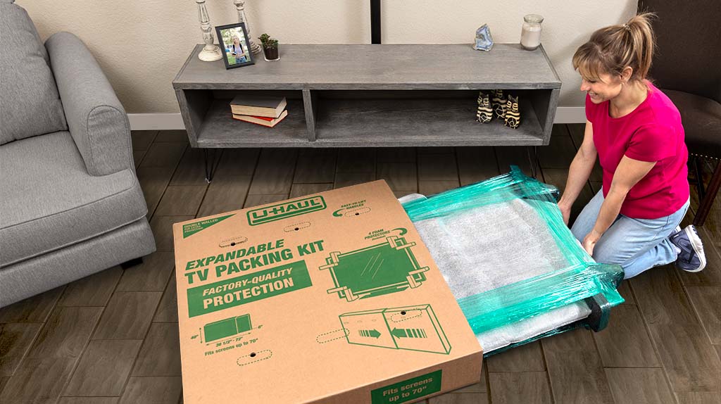 A woman carefully puts her TV inside her U-Haul TV moving box, so her TV will be extra protected and secure during her move.