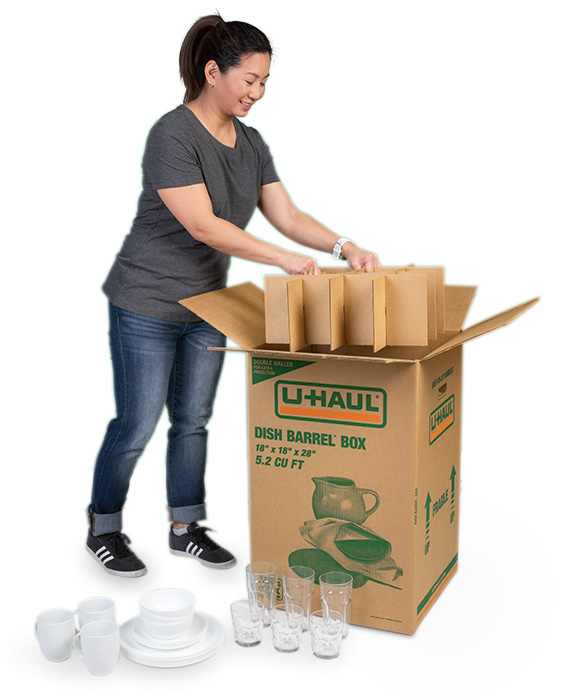 A woman carefully places part of her cell kit inside her dish barrel box. These two U-Haul products pair well together for easy packing and safe moving.
