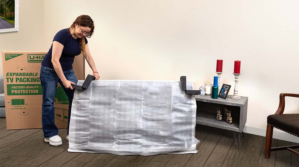 A woman puts on her second foam protection piece onto her TV. The foam protection pieces offer more safety to your TV when moving.