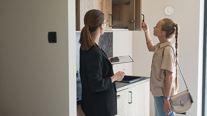 A woman opens a kitchen cabinet to see the inside of it while she’s on her apartment tour with the leasing agent who is standing nearby. Moving Help compiled 25 questions to ask when touring an apartment because these questions can help you determine whether this apartment is a good fit or not.
