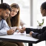 A couple signs official documents as their real estate agent points out where they need to sign. Housing mortgage rates will remain between 6 to 7 percent in 2025.