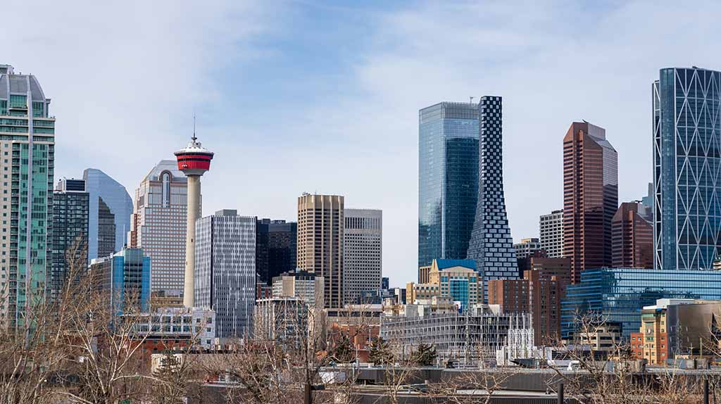 The Calgary Tower is visible in the background of downtown Calgary during a mostly cloudy day.