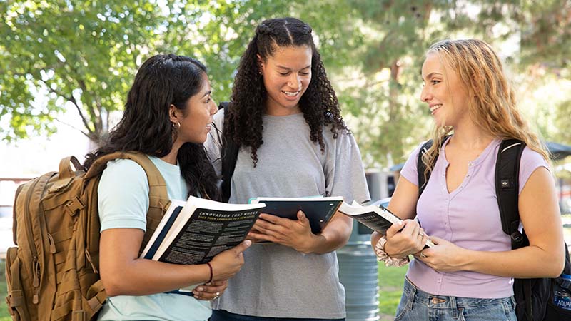 Three female college students stand next to one another as they discuss their fall classes for the upcoming semester as freshmen.