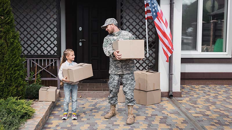 A man in the military carries a box while looking at his daughter, who is also carrying a moving box, as they prepare for a military move.